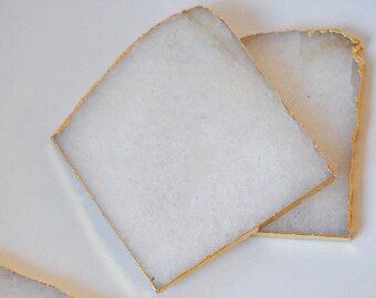 May include: Set of three white agate coasters with gold trim. The coasters are irregularly shaped and have a natural, organic look.