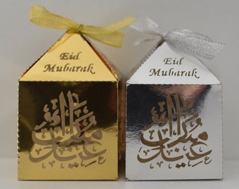 May include: Two small gift boxes, one gold and one silver. Both boxes have the words "Eid Mubarak" printed on the top and a decorative Arabic calligraphy design on the front.