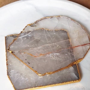 May include: Two white agate coasters with gold trim. The coasters are stacked on top of each other.
