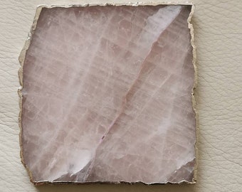 May include: A light pink agate coaster with a gold metal trim. The coaster has a natural, irregular shape.