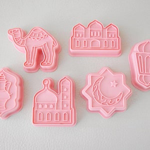 Peut inclure: Ensemble de six emporte-pièces en plastique rose aux motifs islamiques. Les emporte-pièces comprennent un chameau, une mosquée, une lanterne, un croissant de lune et une étoile, une théière et un bâtiment avec un dôme.