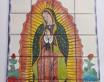 May include: A hand-painted tile mural depicting Our Lady of Guadalupe. The image features a central figure in a green robe and a yellow halo, surrounded by a radiant light. Colorful roses in red, blue, and yellow adorn the border, with a blue border.