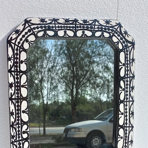 Puede incluir: Un espejo octogonal blanco con un diseño geométrico negro alrededor del marco. El espejo refleja un árbol y un coche.