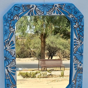 May include: A blue and white ceramic mirror with a floral design. The mirror is octagonal and has a bevelled edge. The floral design is in a traditional Mexican style.