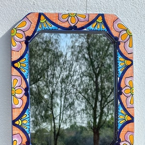 May include: A rectangular mirror with a colorful, hand-painted ceramic frame. The frame features a repeating pattern of pink, orange, yellow, blue, and green flowers and geometric shapes.
