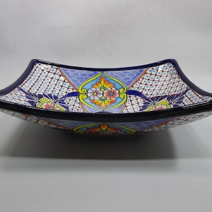 May include: A square ceramic serving bowl with a navy blue rim and a decorative floral pattern. The bowl features a blue, white, red, and yellow design. The bowl's edges curve upwards, creating a unique shape.