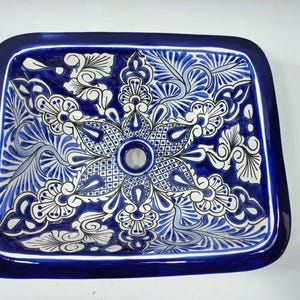 Könnte beinhalten: Rechteckiges Keramikwaschbecken mit einem lebendigen blau-weißen Blumendesign. Das Waschbecken hat einen dunkelblauen Rand und ein zentrales Abflussloch. Das komplizierte Muster umfasst stilisierte Blumen und Blätter und schafft ein dekoratives Badezimmeraccessoire.