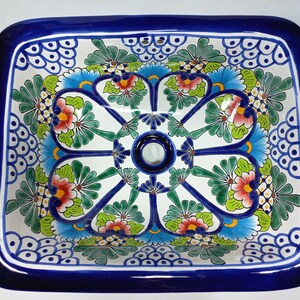 May include: A square ceramic sink with a blue rim and a floral design in shades of blue, green, red, and yellow.