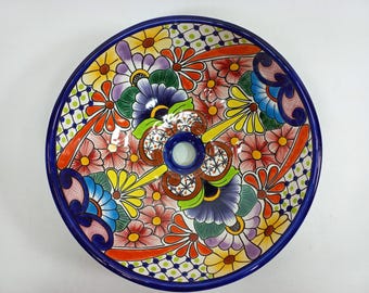 Op de afbeelding: Een kleurrijk keramiek wastafel met een bloemenontwerp in tinten blauw, groen, geel, rood en roze. De wastafel is rond en heeft een afvoergat in het midden.