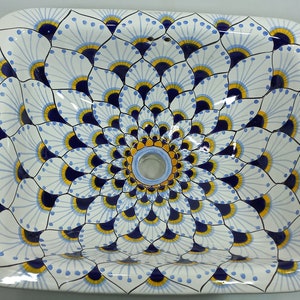 Pode incluir: Uma pia de cerâmica branca com um design floral azul e amarelo. A pia tem um ralo circular no centro.