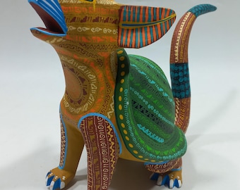 May include: A vibrantly painted wooden sculpture of a coyote in a seated position, with its mouth open as if howling. The coyote features intricate patterns in shades of orange, green, blue, and brown. The sculpture is a folk art piece.
