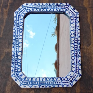 May include: A rectangular mirror with a decorative blue and white patterned frame. The mirror reflects a blue sky with clouds and a portion of a building. The frame has an octagonal shape.