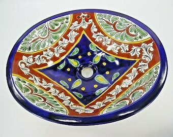 May include: Oval ceramic sink with a vibrant hand-painted design. The sink features a deep blue interior with a central drain, surrounded by a pattern of red, green, white, and yellow floral and geometric motifs. The rim is a solid, glossy blue.