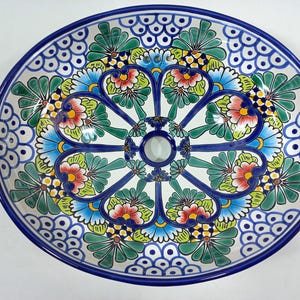 May include: A round, hand-painted ceramic plate with a vibrant floral design. The plate features a white base with a central floral pattern in blue, green, red, and yellow. The rim is a deep blue, and the plate is likely used for serving food.