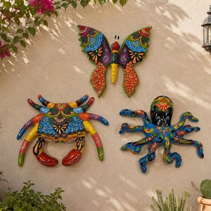 May include: Three colorful wall-mounted sculptures featuring a butterfly, a crab, and an octopus. Each piece is decorated with intricate, vibrant patterns in shades of red, blue, yellow, green, and black, showcasing a glossy, hand-painted finish.