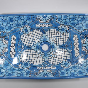 Op de afbeelding: Een rechthoekige keramische gootsteen met een blauw en wit bloemenpatroon. De gootsteen heeft een enkel afvoergat in het midden.