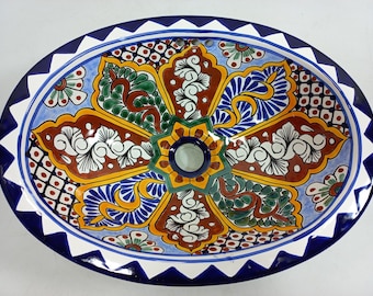 May include: Oval ceramic sink with a colorful floral design in shades of blue, green, yellow, red, and white. The sink has a white rim with a blue and white scalloped edge.