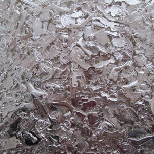 May include: A large collection of silver-toned metal charms in various shapes and sizes. The charms are scattered randomly on a white surface.