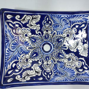 Op de afbeelding: Een blauwe en witte keramische wastafel met een bloemenpatroon. De wastafel heeft een vierkante vorm met afgeronde hoeken en een enkel afvoergat in het midden.