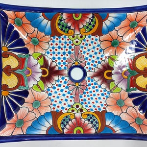 May include: Rectangular ceramic sink with a vibrant floral design. The sink features a deep blue border and is adorned with colorful flowers in shades of orange, blue, purple, and red. The center has a white drain and a dotted pattern.