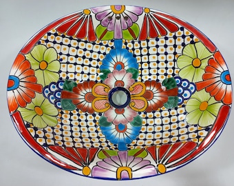 May include: Oval ceramic sink basin with a vibrant floral design. The hand-painted sink features a red, blue, green, and yellow color palette. The sink has a central drain and is decorated with flowers and geometric patterns.