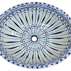 May include: A white ceramic sink with a blue and white geometric pattern. The sink has a round shape and a drain hole in the center.
