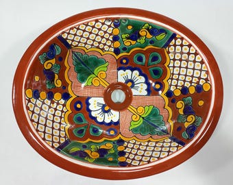 May include: A ceramic sink with a colorful floral pattern in shades of blue, green, yellow, and white on a red background. The sink is oval shaped and has a drain hole in the center.