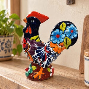 May include: A ceramic rooster figurine featuring a glossy finish with a vibrant, multi-colored floral pattern. The rooster has a bright red comb, a dark blue head and neck, and a tail decorated with blue, orange, and yellow flowers.