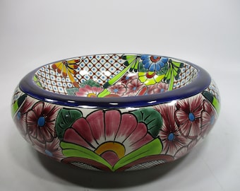 Op de afbeelding: Een grote, ronde keramische kom met een kleurrijk bloemenontwerp. De kom is beschilderd met roze, rode, gele, groene, blauwe en witte bloemen. De rand van de kom is beschilderd met een donkerblauwe band.
