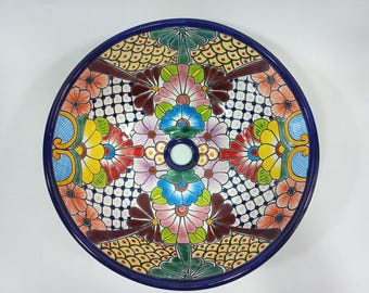 Op de afbeelding: Een ronde keramische wastafel met een kleurrijk bloemenontwerp. De wastafel heeft een blauwe rand en een wit midden met een afvoergat. Het bloemenontwerp bevat een verscheidenheid aan kleuren, waaronder rood, geel, blauw, groen en roze.