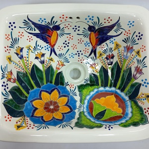 May include: A white ceramic bathroom sink with a floral design featuring hummingbirds, flowers, and leaves. The sink has a drain hole in the centre.