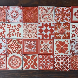 Puede incluir: Una colección de veinticuatro azulejos cuadrados de cerámica dispuestos en cuadrícula. Cada azulejo presenta un patrón distinto en blanco y rojo terracota, incluyendo motivos florales, formas geométricas, mandalas y volutas.