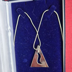 May include: A silver necklace with a triangular pendant featuring a cut-out design. The necklace is displayed in a blue velvet box.
