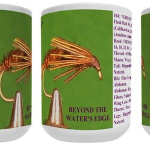 May include: A white ceramic mug with a green background and a detailed illustration of a fly fishing lure. The text "GDB-CIV" is printed on the mug. The back of the mug has a description of the fly fishing lure, including the name, size, and materials used.