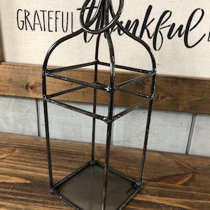 May include: Black metal lantern with a square base and a ring handle. The lantern has a rustic, distressed finish.