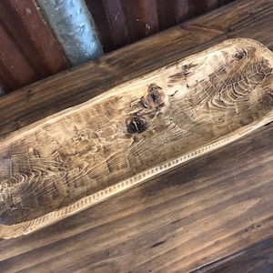 May include: A rustic wooden dough bowl with a natural wood finish. The bowl has a slightly rounded shape and a smooth, polished surface.