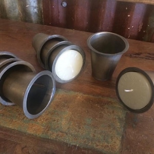 May include: A set of four gray metal candle holders, each with a different size and shape. The candle holders are arranged on a wooden surface.