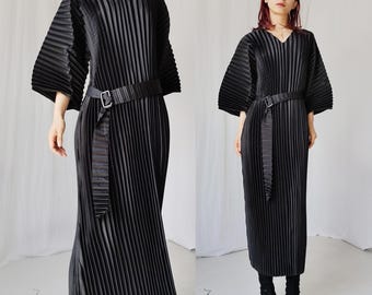 Vestido longo preto plissado minimalista com decote em V, manga quimono, modelo kaftan oversized, da Issey Miyake, modelo Pleats Please.