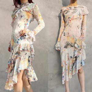 Op de afbeelding: Twee jurken met lange mouwen en een gelaagd, gerimpeld ontwerp. De jurken hebben een aquarelachtige print in tinten geel, blauw en roze. De stof lijkt doorschijnend, met een asymmetrische zoom en uitlopende mouwen. De jurken zijn elegant en artistiek.