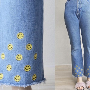 May include: Light blue denim jeans with a frayed hem. The jeans are decorated with yellow smiley faces near the bottom of the legs. The jeans have a classic five-pocket design.