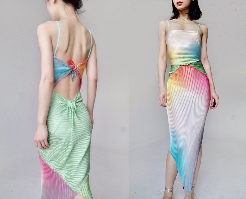 May include: A colorful pleated dress with a halter top and open back. The dress features a rainbow gradient of colors, including green, blue, pink, and yellow. The skirt has an asymmetrical hemline and a knot detail at the back.