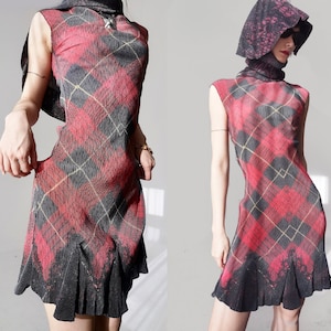 May include: A sleeveless dress in a red, black, and yellow plaid pattern, featuring a pleated skirt and high neck. The model is also wearing a matching hood. The dress is a unique fashion statement.