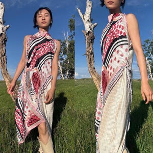 Könnte beinhalten: Ein ärmelloses, plissiertes Kleid mit hohem Kragen. Das Kleid hat ein Muster aus roten, schwarzen und weißen Formen auf hellrosa Hintergrund. Das Kleid ist knielang und hat einen fließenden, asymmetrischen Saum.