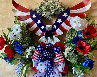 May include: A patriotic wreath featuring a metal eagle with red, white, and blue wings and a matching bow. The wreath is adorned with red, white, and blue flowers and greenery, perfect for celebrating Independence Day.