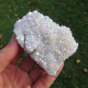Puede incluir: Un c&uacute;mulo de cristales de cuarzo blanco iridiscente con un brillo arco&iacute;ris. Los cristales est&aacute;n agrupados en una formaci&oacute;n natural rugosa.