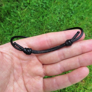 May include: A black cord necklace with a simple knot closure.