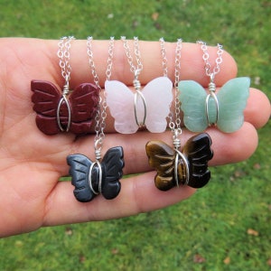 May include: Five silver chain necklaces with butterfly-shaped pendants made of different gemstones. The pendants are wrapped in silver wire. The gemstones are red, pink, green, black, and brown.