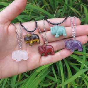 May include: Five silver chain necklaces with elephant pendants made of different gemstones. The pendants are in the colors of rose quartz, tiger's eye, red jasper, amethyst, and green aventurine.