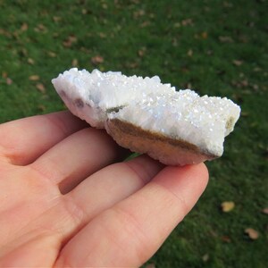 Puede incluir: Un c&uacute;mulo de cristales de cuarzo blanco iridiscente con una base natural y rugosa. Los cristales est&aacute;n agrupados en una formaci&oacute;n natural, creando una pieza &uacute;nica y hermosa.