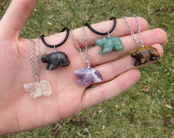 May include: Five necklaces with bear pendants made of different types of stones. The pendants are in the colors of clear, black, green, purple, and brown.